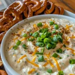 Close-up view of a creamy pretzel dip with green onion garnish next to pretzels.