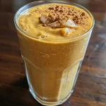 Close-up view of a creamy pumpkin protein smoothie in a glass, topped with a sprinkle of cinnamon.