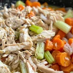 Close-up of juicy shredded chicken with vegetables in a slow cooker.