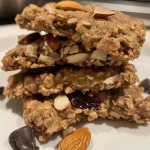 A close-up side view of a plate of oatmeal breakfast cookies, showcasing their chewy texture and mix of ingredients.